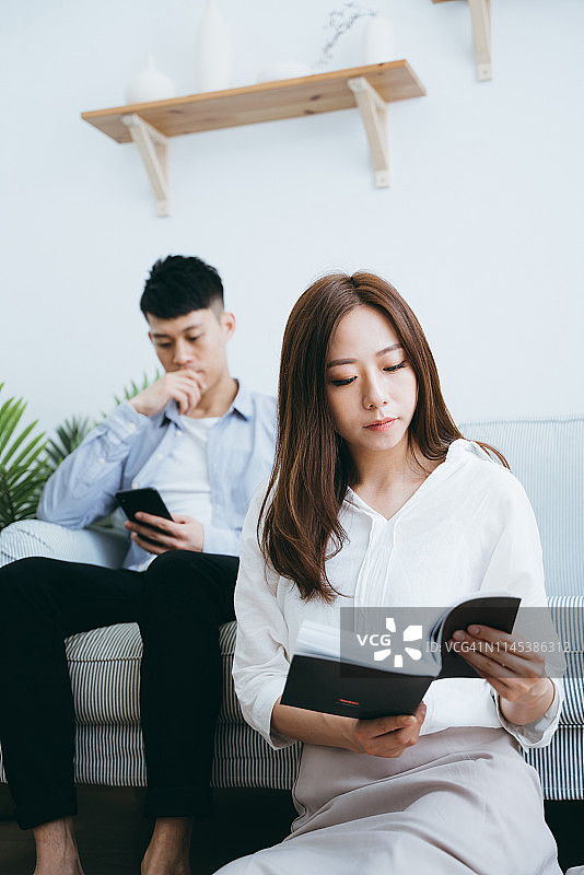 在客厅里各自玩手机看书、缺乏交流的夫妇图片素材