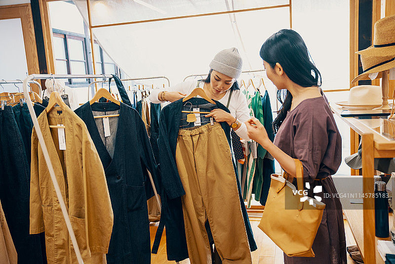 零售店员帮助中年女性顾客在精品店选购服装图片素材