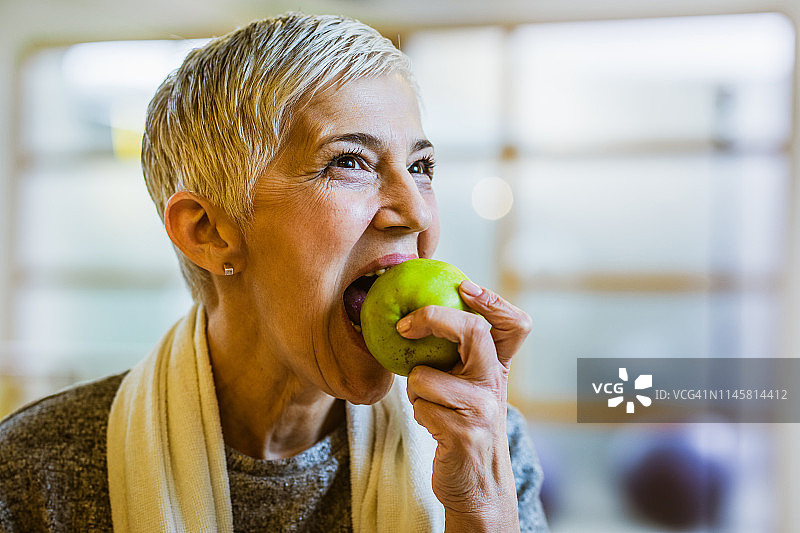 在健身俱乐部锻炼后吃苹果的资深健美女性图片素材