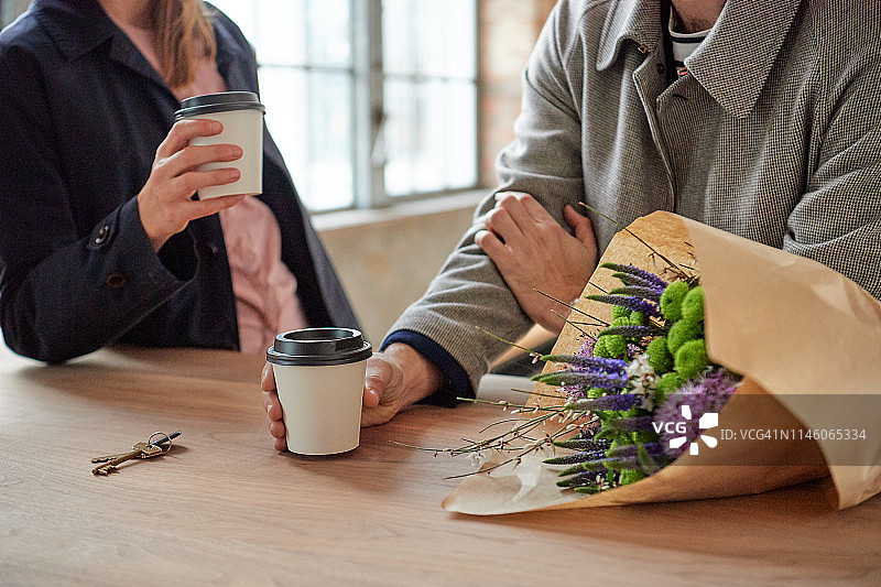 一男一女在他们的新公寓里交谈，喝着外卖咖啡，欣赏着美丽的花束图片素材