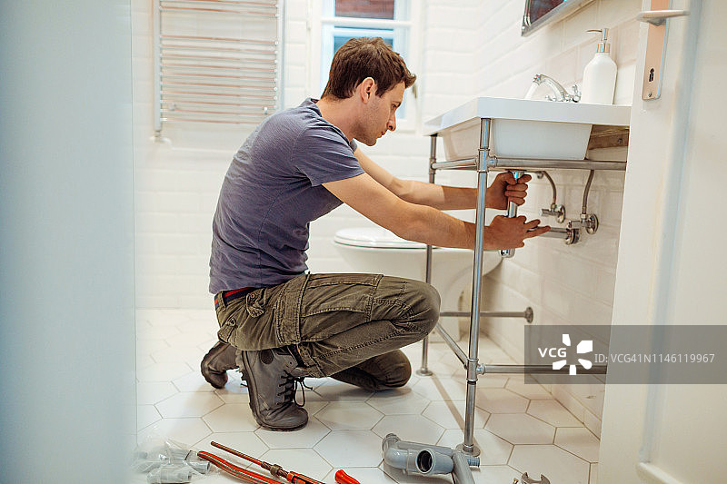 年轻男子正在修理浴室水槽下的漏水图片素材