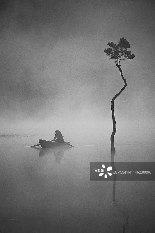 雾气蒙蒙的湖上钓鱼船上的钓鱼人图片素材