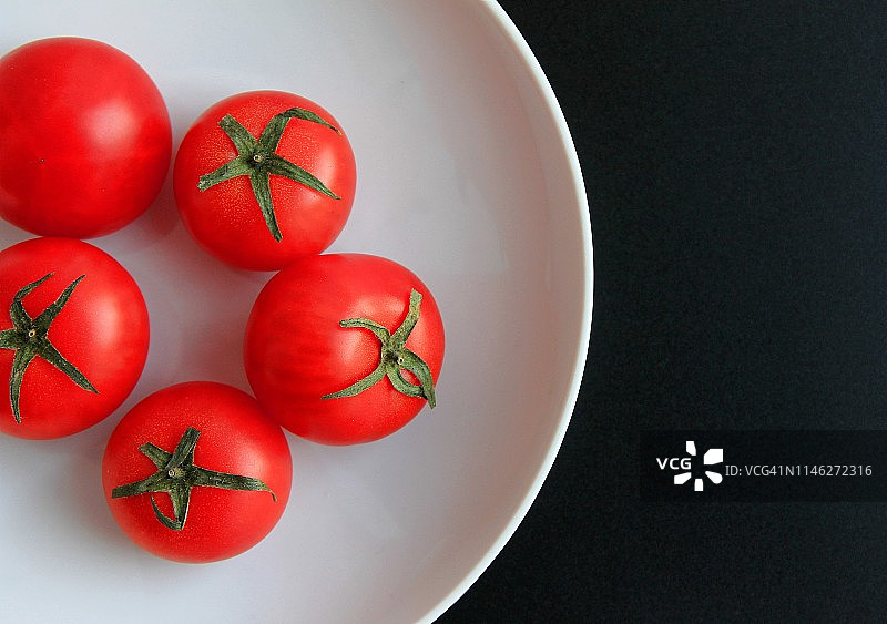 黑色背景白色盘子里的红色番茄图片素材