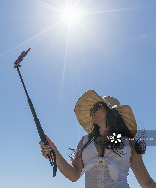 仰视角度拍摄的用自拍杆的女人图片素材