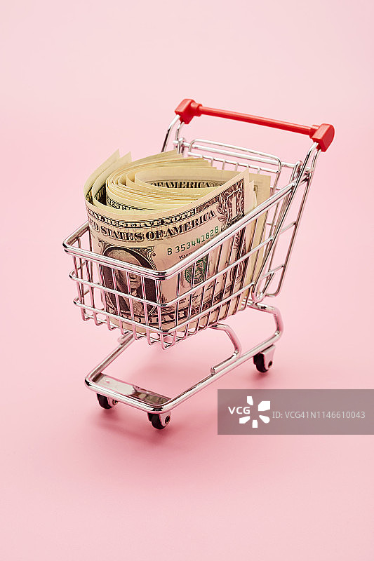 粉色背景上的购物车和美元纸币静物图片素材