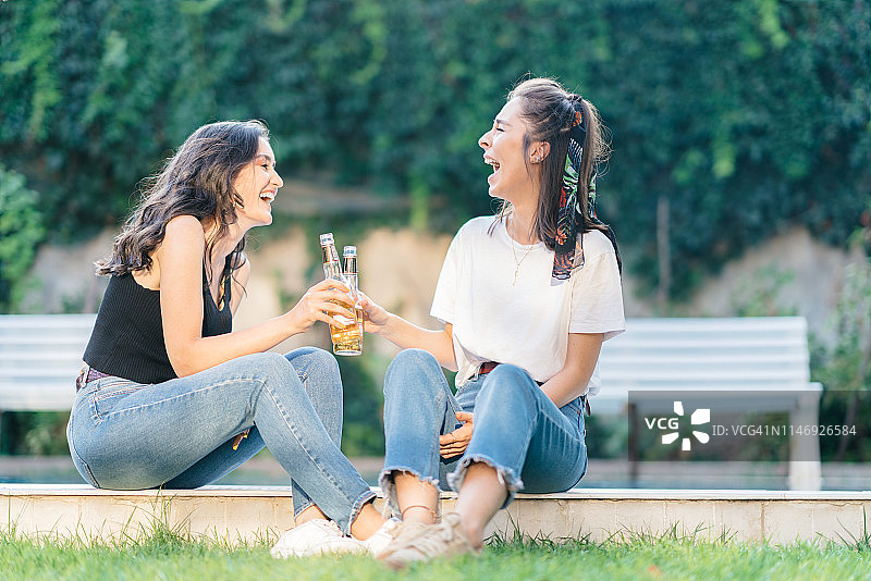 两位女性朋友在游泳池边喝啤酒庆祝图片素材