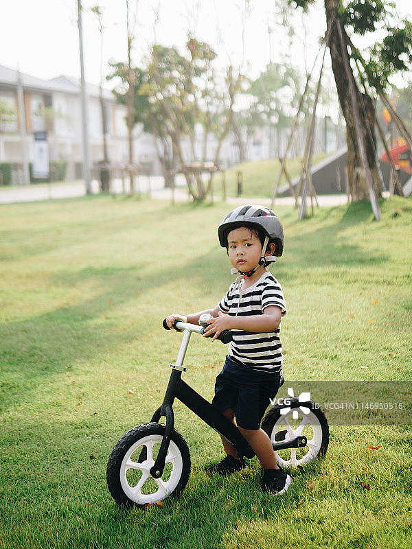 阳光明媚的泰国公园里，戴着运动头盔的亚洲小男孩骑着自行车图片素材