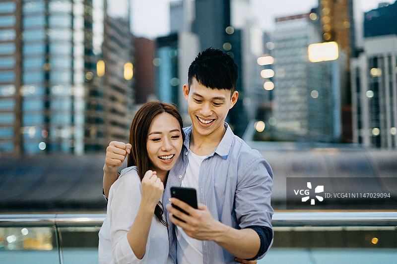 幸福的夫妻在城市中用智能手机分享好消息，笑容满面图片素材