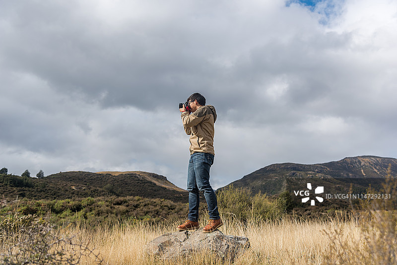 男人在被自然景观环绕的岩石上拍照图片素材