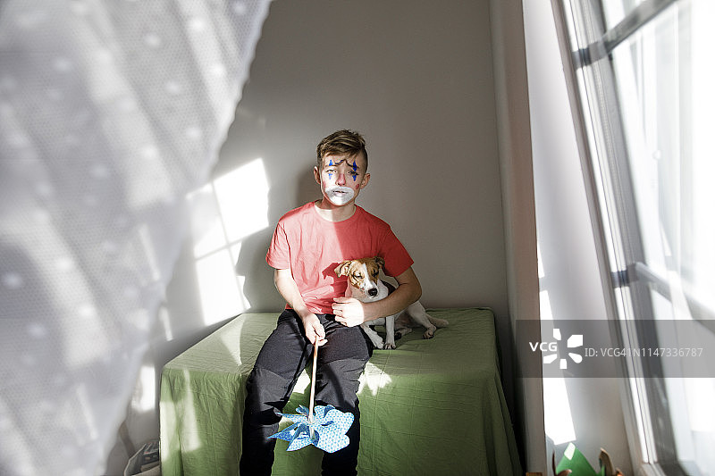 男孩在家中扮成小丑，与狗和风车合影的肖像照图片素材