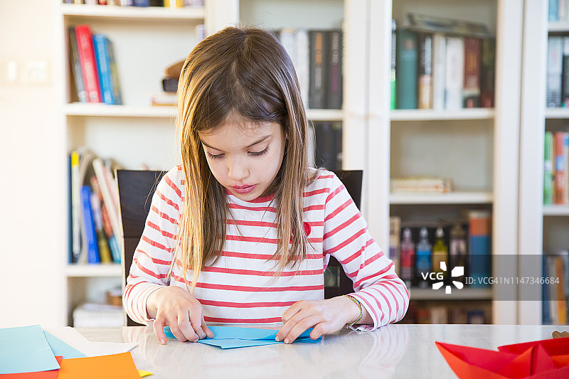 女孩在家里的桌子上摆弄纸图片素材