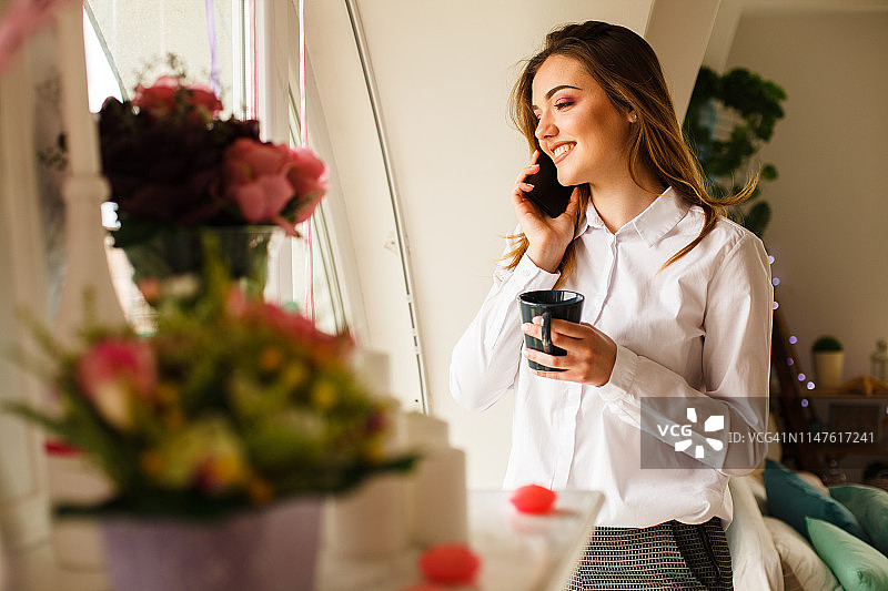 年轻女商人在家窗边打电话图片素材