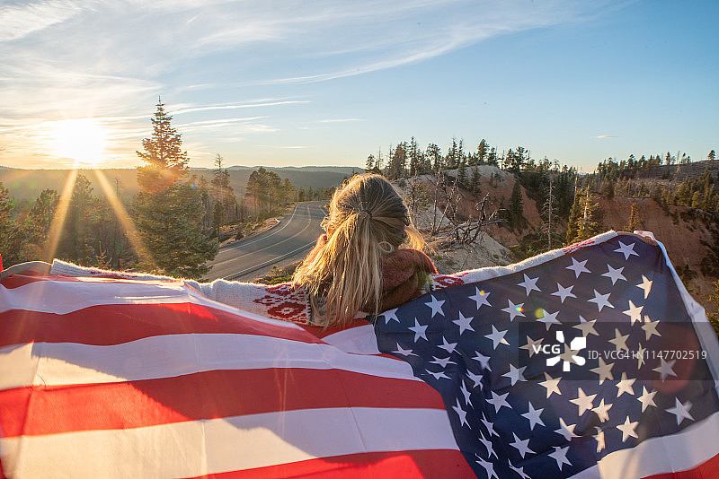 在美国旅行的女孩手持美国国旗，欣赏自然风光；日落时分，女子张开双臂挥舞美国国旗图片素材