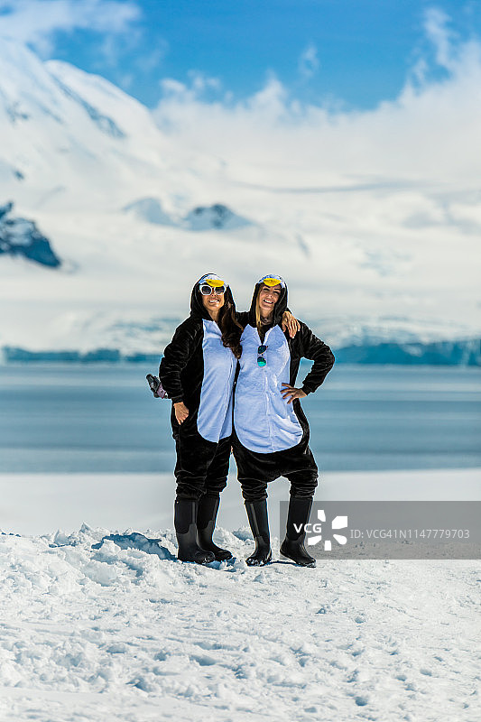 两名美国女游客身穿企鹅连体服在南极冰川上合影图片素材