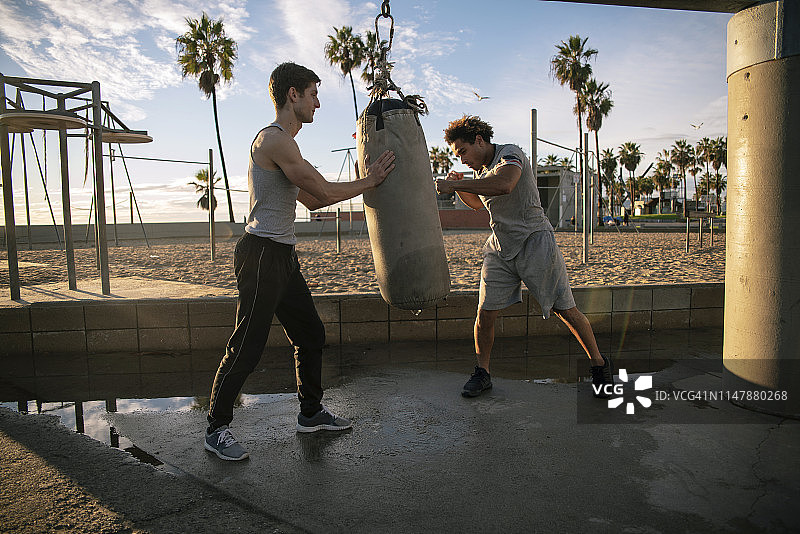 两位朋友在户外运动区进行拳击训练，一位是西班牙裔，一位是白人图片素材