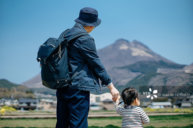 阳光下，年轻的亚洲父女漫步油菜花田图片素材