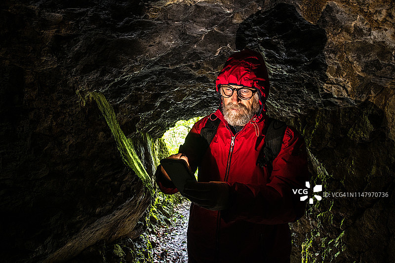 年长的男人探索洞穴并看手机图片素材