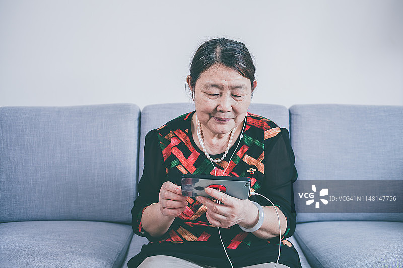 年长的女人戴着耳机在室内使用手机图片素材