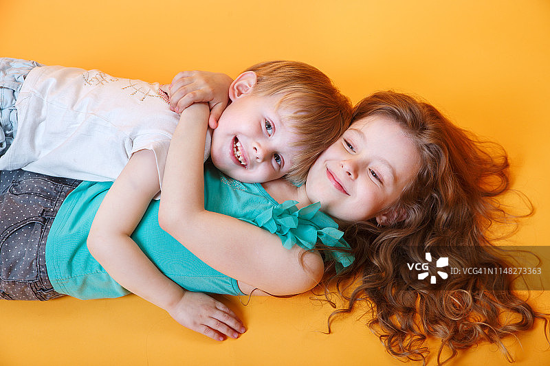 快乐的弟弟和妹妹躺在彩色黄色背景上图片素材