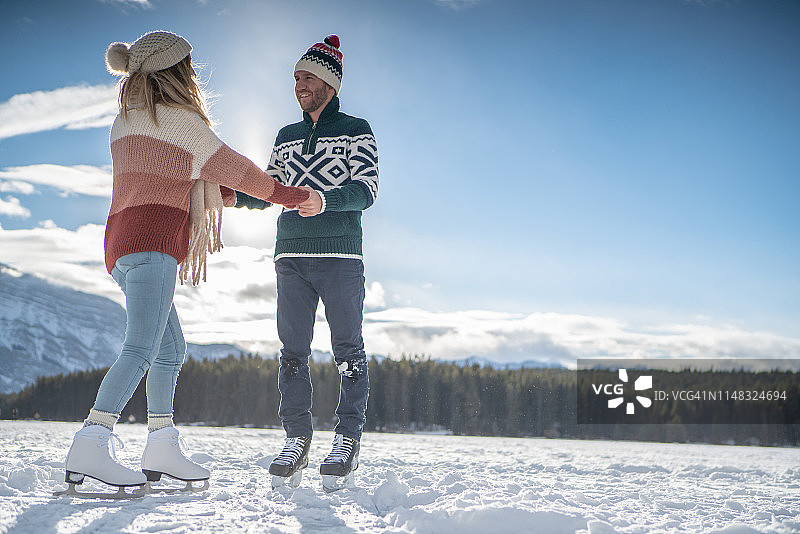 快乐的年轻夫妇手牵手在结冰的湖面上滑冰，享受冬季乐趣图片素材
