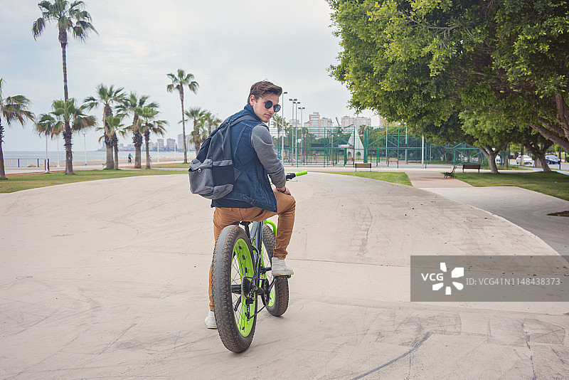 年轻英俊的男人在公园里摆姿势骑自行车图片素材