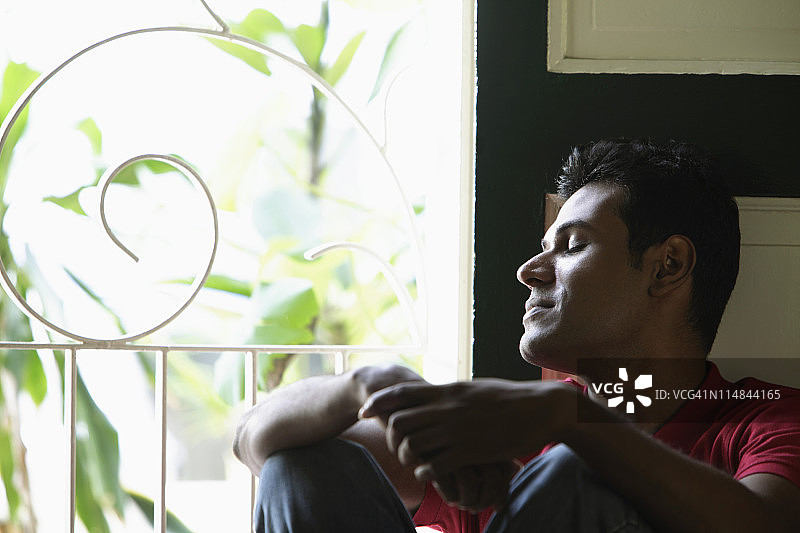 闭着眼睛坐在窗边的印度男人图片素材
