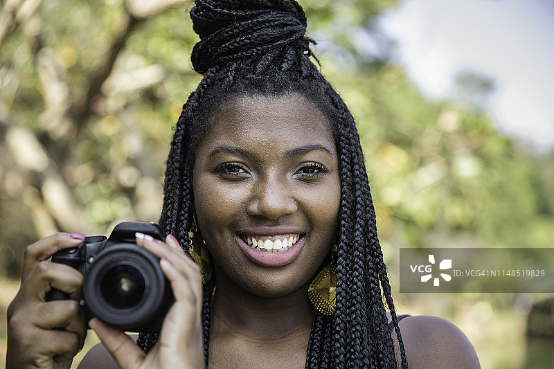 年轻的非洲裔女人在公园里用单反相机拍照图片素材