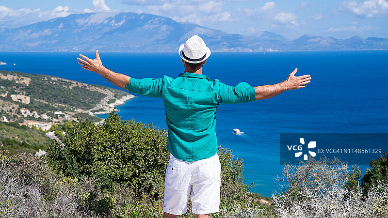 戴帽子的男人在希腊扎金索斯山顶张开双臂看海图片素材