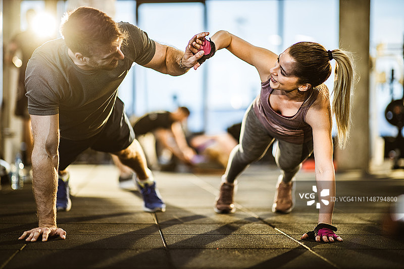 在健身房合作做俯卧撑的快乐运动情侣图片素材