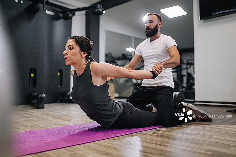 健身教练帮助身材健康的女子做拉伸运动图片素材