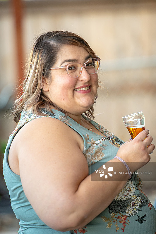 面带微笑的中年妇女看着镜头，拿着一杯啤酒图片素材