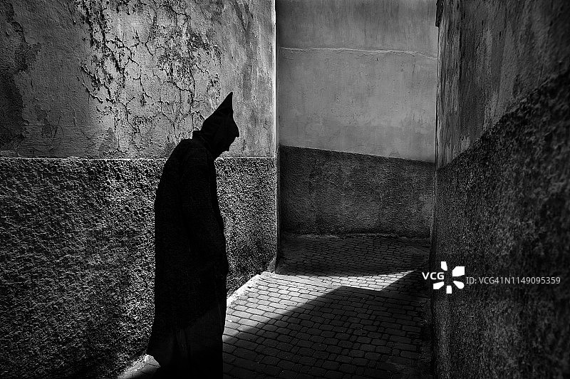 身穿阿拉伯长袍站在昏暗小巷中的男人图片素材