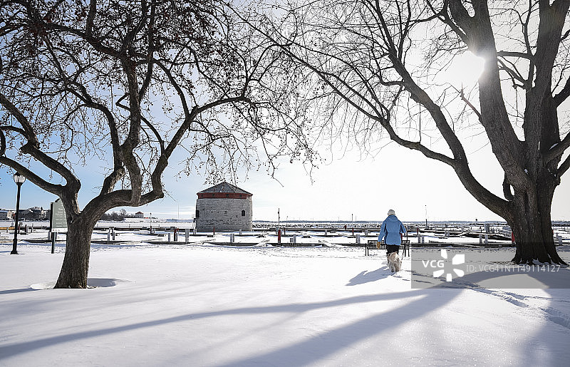 在下雪天，女人在海滨的塔楼和码头附近遛狗图片素材