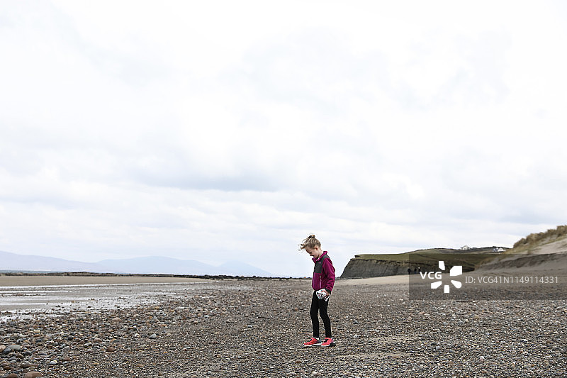 站在爱尔兰岩石海滩上的年轻卷发金发女孩图片素材