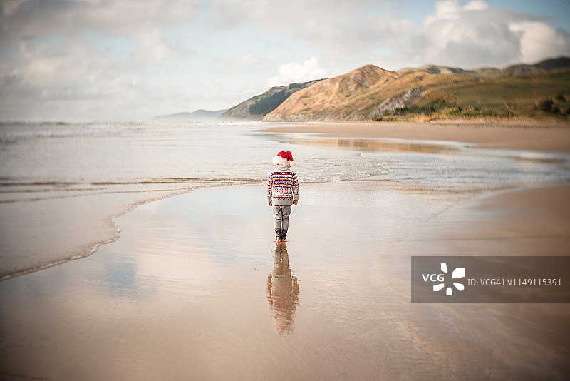 戴着红色节日帽的孩子在海滩上行走图片素材