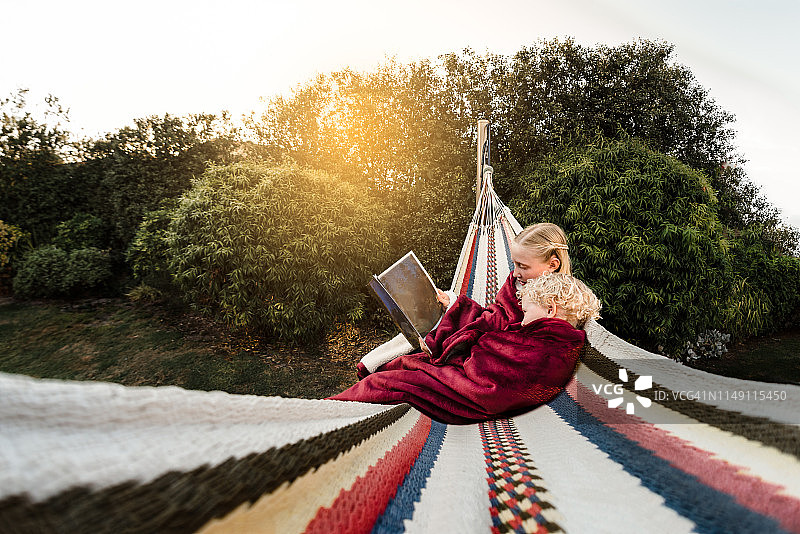 姐姐在吊床上给弟弟读书图片素材
