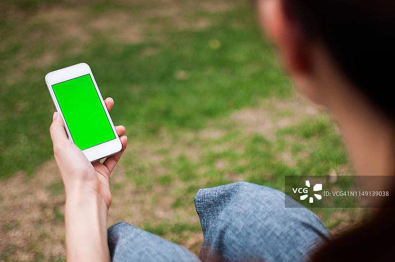 年轻女人在户外手持带绿屏的手机图片素材