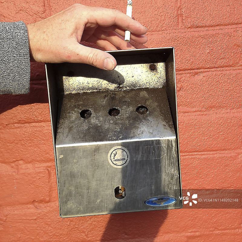 公共烟灰缸上的香烟与手图片素材