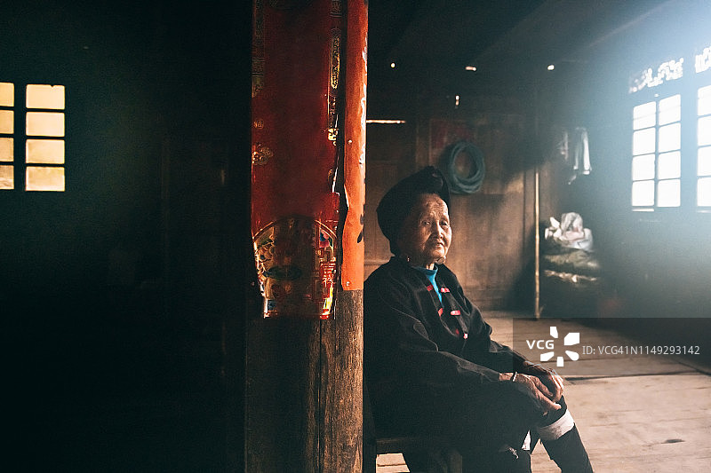 黑暗的房间里，一个中国老妇人坐在凳子上图片素材