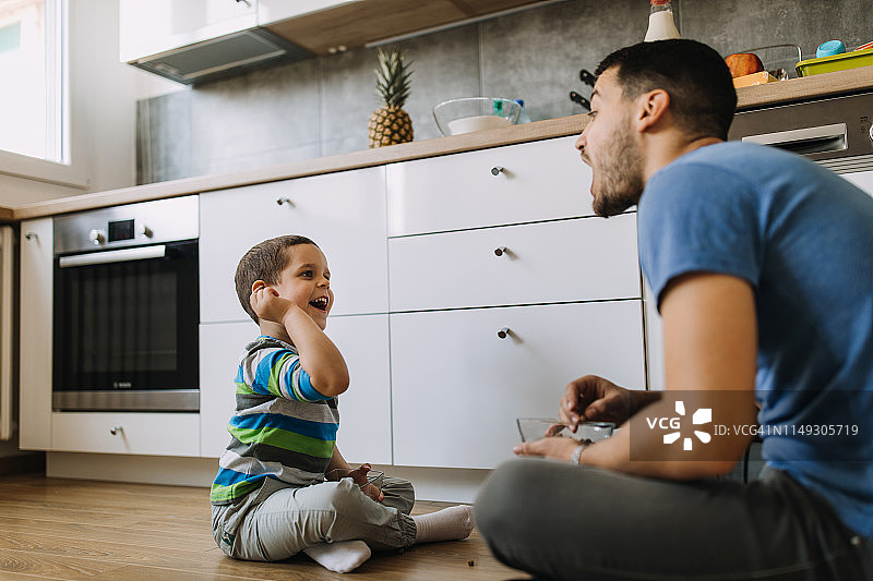 父子坐在厨房地板上玩食物图片素材
