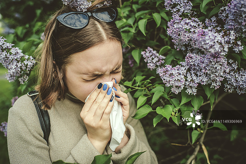 春天公园里因花粉过敏打喷嚏，正在擦鼻子的女孩图片素材