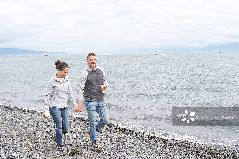 夫妇手牵手在阿拉斯加岩石岸边喝咖啡图片素材