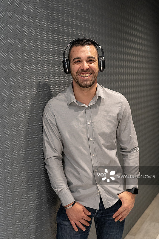 年轻商人戴耳机在灰色背景前图片素材
