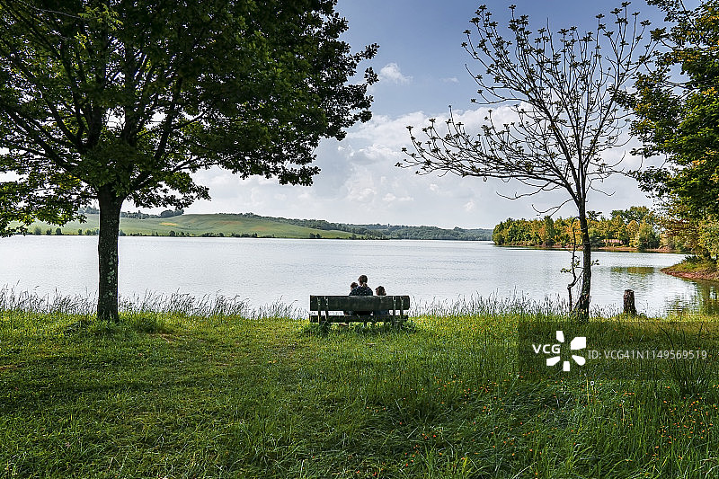 年轻母亲和两个孩子坐在湖边的长椅上图片素材