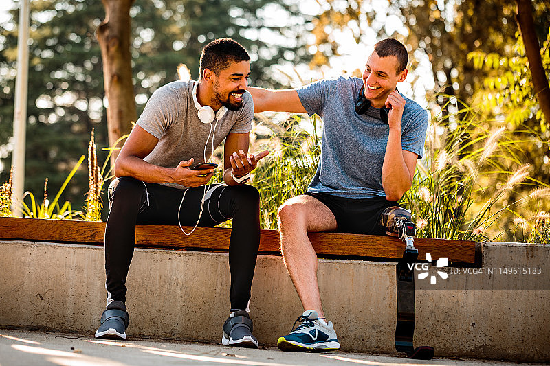 残疾运动员与非裔朋友在城市公园长椅上图片素材