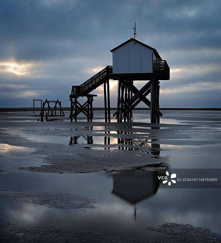 黎明时分海滩上的退潮湖畔小屋，阴云密布，位于德国石勒苏益格-荷尔斯泰因瓦登海国家公园的圣彼得-奥尔丁图片素材