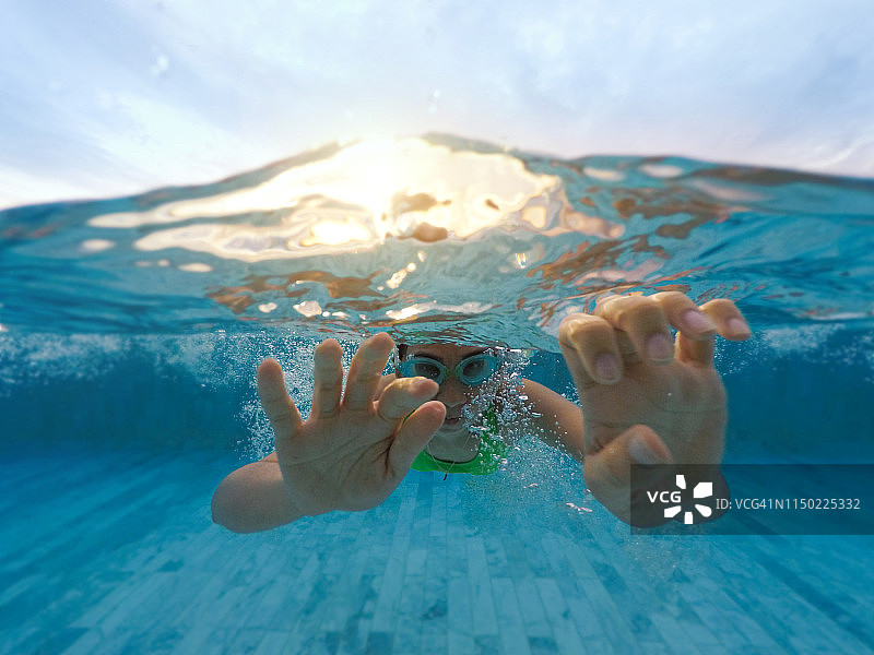 年轻女子在水下游泳，阳光反射在游泳池中图片素材