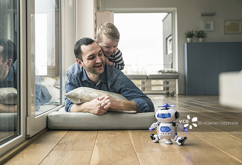 兴奋的父子躺在家里床垫上看玩具机器人图片素材