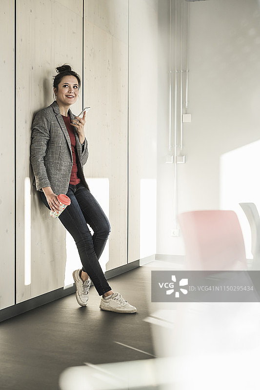 在办公室靠墙使用手机的女商人图片素材