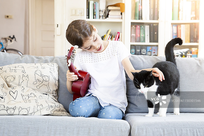 坐在沙发上抚摸猫咪的尤克里里女孩图片素材